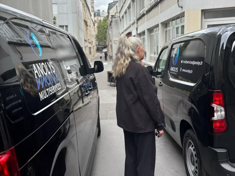 Deux utilitaires noirs au logo ANOLYS Multiservices garés dans une rue, une personne de dos entre les deux